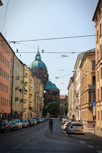 Cars on road by buildings against sky in city