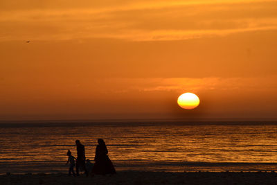 Silhouette people on beach against orange sky