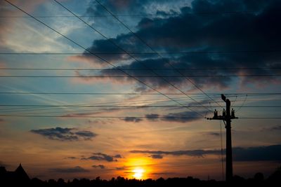 Silhouette electricity pylon against dramatic sky during sunset