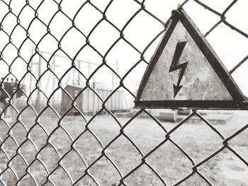 Close-up of hazard sign on chainlink fence