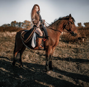 Full length portrait of young woman riding horse on field