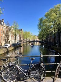 Bicycles on canal in city against clear blue sky