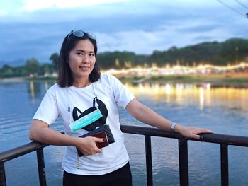 Portrait of woman standing by railing against lake