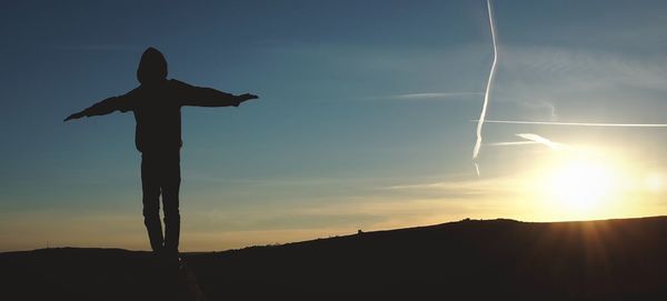 Silhouette boy standing against sky during sunset