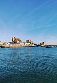 Buildings by sea against blue sky