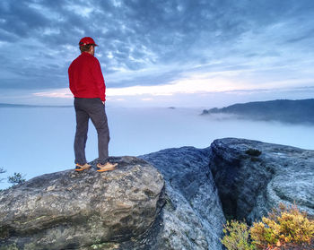 Nature misty show. guy stand on top of mountain. hiking trip in rocks and forest. beautiful nature