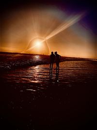 Silhouette people on beach against sky during sunset