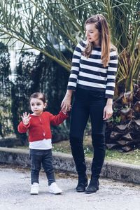 Full length of mother with daughter standing on footpath against trees