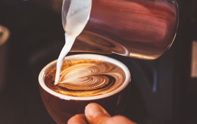 Cropped image of person pouring milk in coffee with heart froth