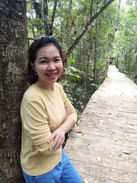 Portrait of smiling woman standing on footpath against trees in forest