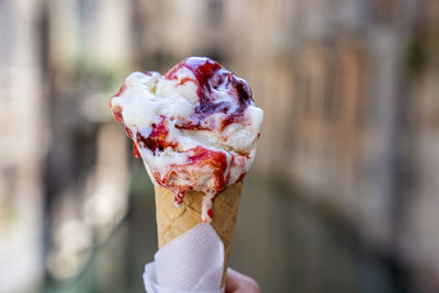 Hand holding delicious melting strawberry gelato ice cream cone