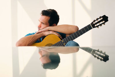 Man looking away while sitting with guitar at home