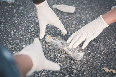 Cropped hands wearing protective gloves while picking plastic bottle from road