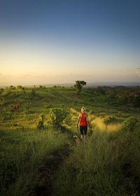 Rear view of woman walking on field against sky during sunset