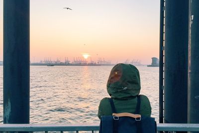 Woman standing by sea against sky during sunset