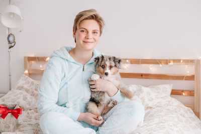 Portrait of young woman with dog sitting on bed