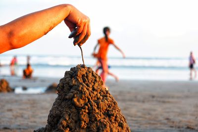 Cropped hand making sandcastle at beach against clear sky