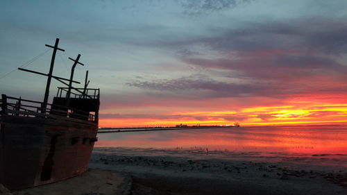 Wooden boat moored at beach against dramatic sky during sunset