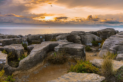 Rocks on sea shore against sky during sunset