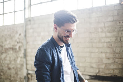 Young man looking away while standing against wall