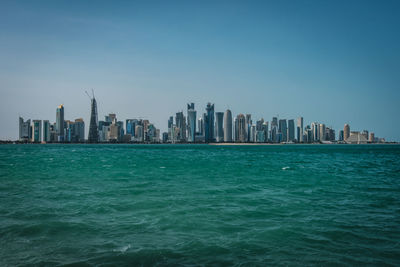 Sea by city buildings against clear sky