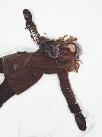 High angle view of young woman with arms outstretched lying down on snow covered field