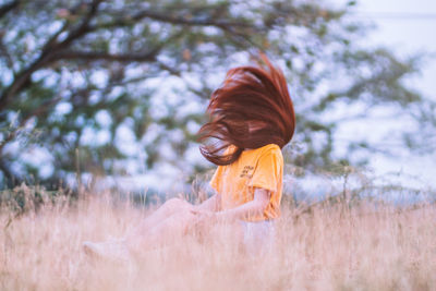 Woman with tousled hair sitting on field