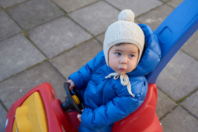 Cute toddler is riding his toy scooter and push car in the back yard