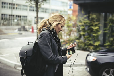 Side view of mid adult businesswoman holding smart phone while walking on city street