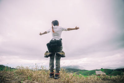 Low angle view of woman with arms outstretched standing on mountain against sky