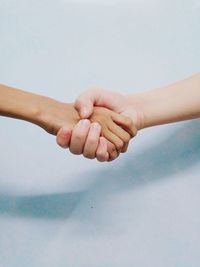 Cropped image of people shaking hands by wall