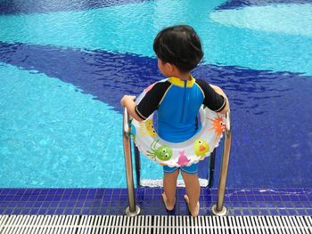 Rear view of girl in inflatable ring standing on poolside