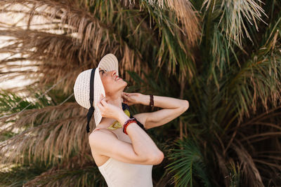 Young woman wearing hat while standing on palm tree