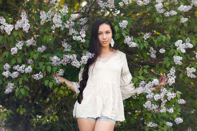 Portrait of beautiful woman standing by flowering plants