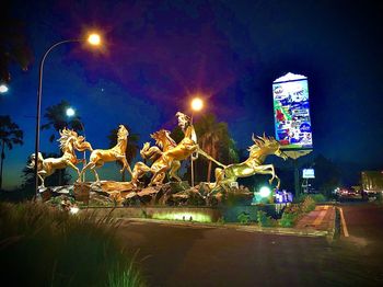 Statue by illuminated street light against sky at night