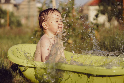 Cute little boy bathing in tub outdoors in garden. happy child is splashing, playing with water