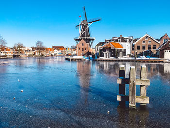 Buildings by canal against clear blue sky