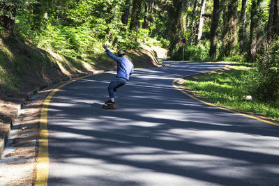 Man riding a longboard on a road through the woods