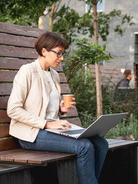 Freelance business woman sits in park with laptop,cup of coffee.urban lifestyle.working remotely.