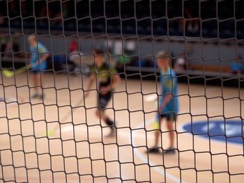 Blurry players of florball. view through protective net of  match. modern surface of florball hall