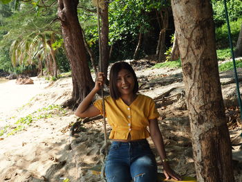 Portrait of smiling woman standing on tree trunk