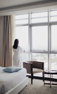 Rear view of woman sitting on bed at home