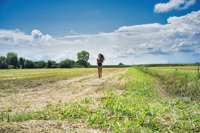 Girl with a black one-piece swimsuit, running in a harvested cornfield.