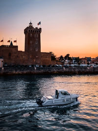 Boat in sea against buildings in city during sunset