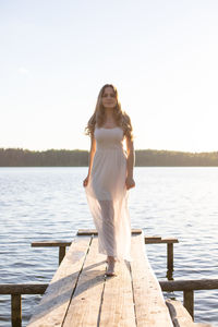 Portrait of young woman walking on jetty by sea against clear sky