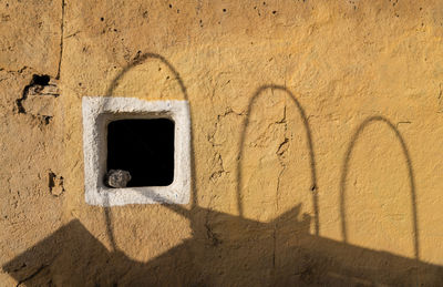 Small window frame on yellow wall with sunlight and shadow