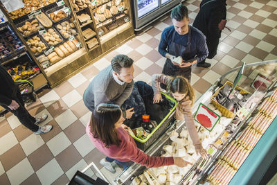 High angle view of family choosing food packets from shelf by owner in store