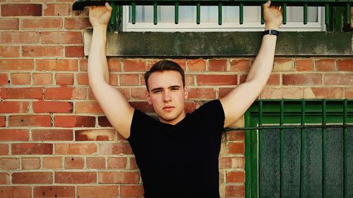 Portrait of young man standing against brick wall