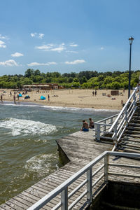 People on pier at beach against sky