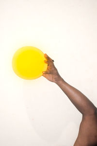 Close-up of hand holding yellow cup over white background